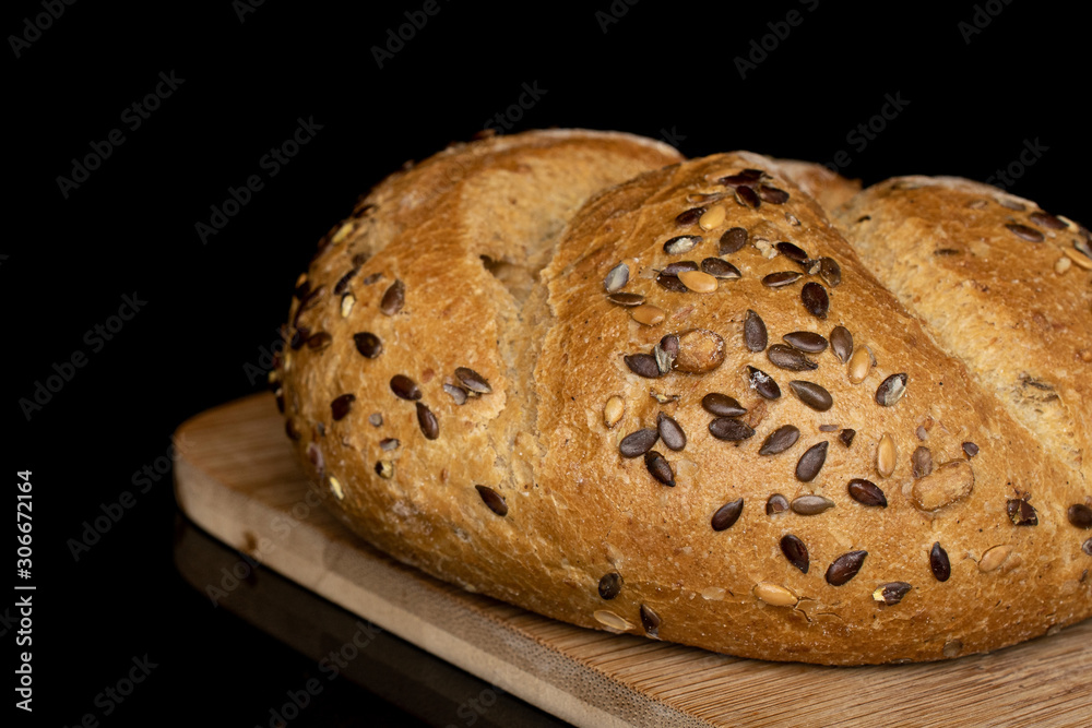 One whole sesame kaiser roll on bamboo cutting board isolated on black glass One whole sesame kaiser roll on bamboo cutting board isolated on black glass