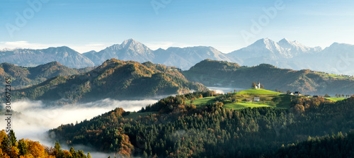 Sveti Tomaz church with low lying fog with the alps in the background during sunrise in fall season Slovenia photo