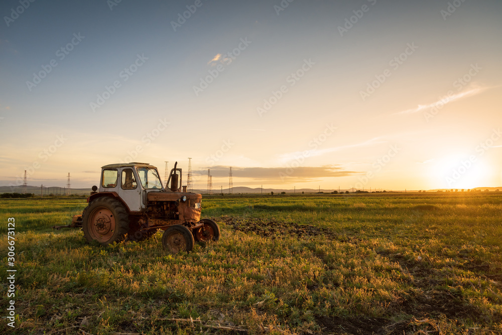 Fototapeta premium Red tractor on golden sunset sky.