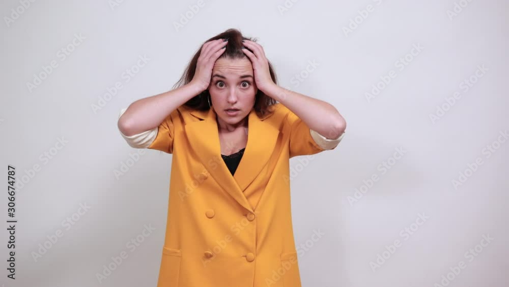 Shocked young woman in yellow jacketkeeping hand on head, looking confused isolated on gray background in studio. People sincere emotions, lifestyle concept. Shocked young woman in yellow jacketkeeping hand on head, looking confused isolated on gray background in studio. People sincere emotions, lifestyle concept.