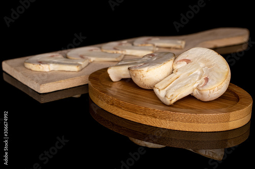 Fototapeta Naklejka Na Ścianę i Meble -  Group of two halves four slices of fresh white champignon on round bamboo coaster on wooden cutting board isolated on black glass