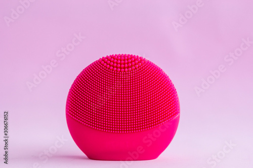 Red silicone facial cleansing brushe with cleansing brush for massaging skin care on pink background. Product for face lifting, anti-aging wrinkles.