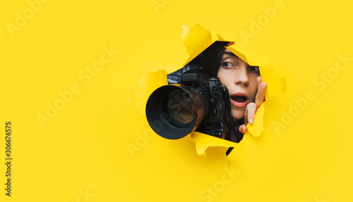 Foto A paparazzi girl with a camera looks out from cover and looks at what is happening with her mouth open