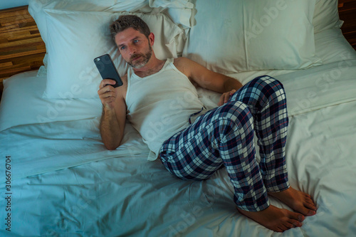 domestic lifestyle high angle portrait of young attractive and relaxed man at home lying on bed wearing pajamas using mobile phone networking and looking social media photo