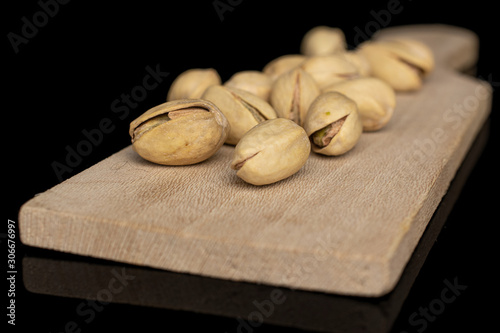 Lot of whole salted pistachio on wooden cutting board isolated on black glass photo