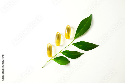 Yellow capsules with green leaves on white background.Vitamins from nature concept.