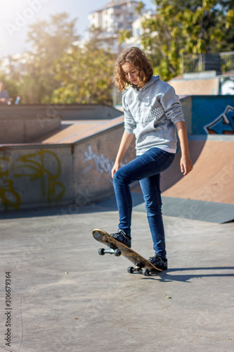 Girl teenager rides on a skateboard. Beautiful fashionable skateboarder in jeans and a hoodie on a ramp. © Anna