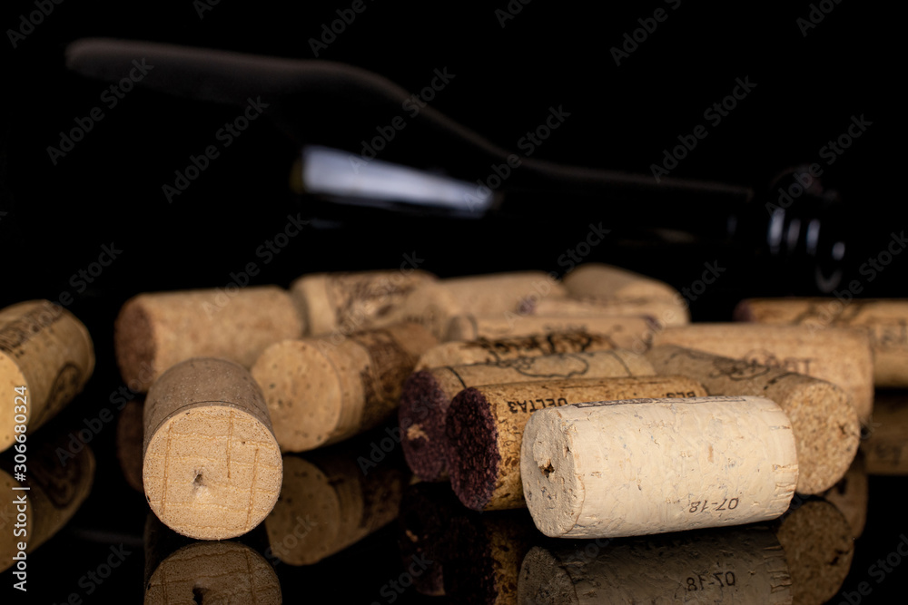 Lot of whole common wine cork  with glass bottle isolated on black glass