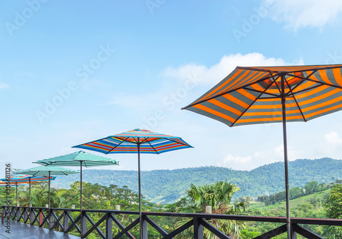 Rows of colorful parasols on wooden balcony terrace with the hill slope and tropical mountains background