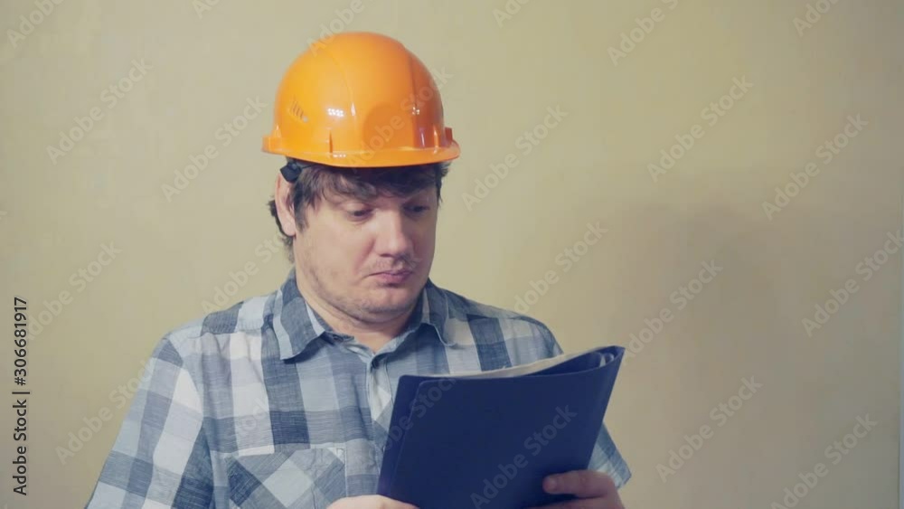 Emotional funny man in a construction helmet with astonishment looks in the documents folder.humorous video portrait of a builder at work Emotional funny man in a construction helmet with astonishment looks in the documents folder.humorous video portrait of a builder at work