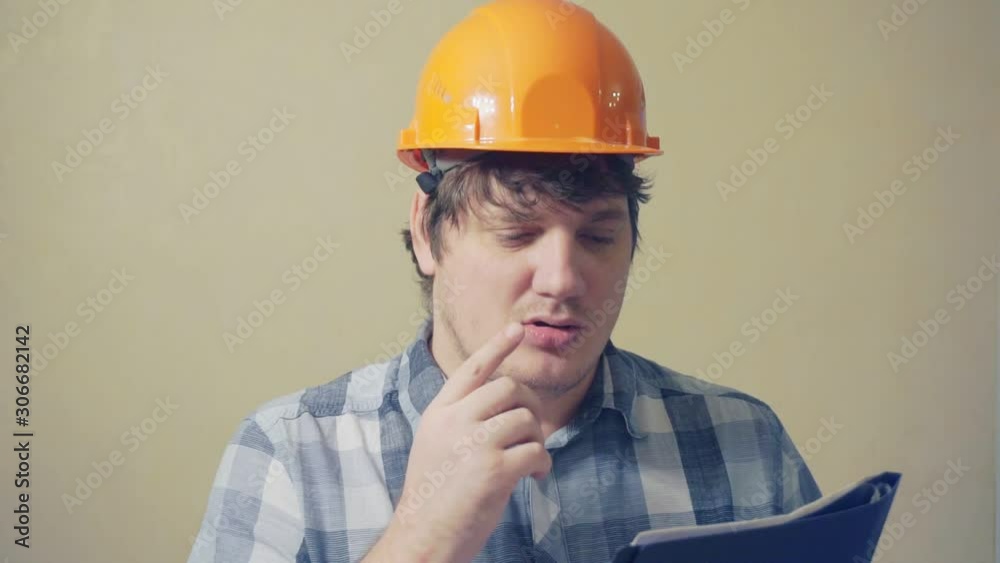 cheerful laughing man in a construction helmet looks in a folder with documents.video portrait of a builder at work cheerful laughing man in a construction helmet looks in a folder with documents.video portrait of a builder at work