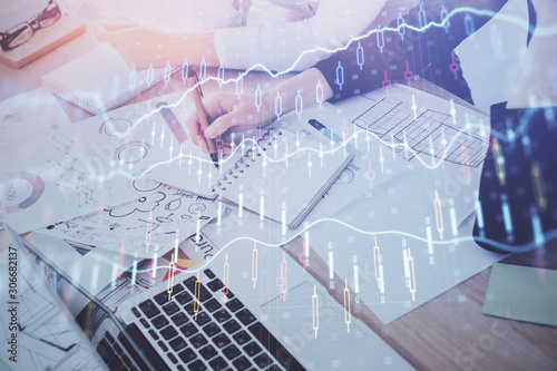 A woman hands writing information about stock market in notepad. Forex chart holograms in front. Concept of research. Double exposure