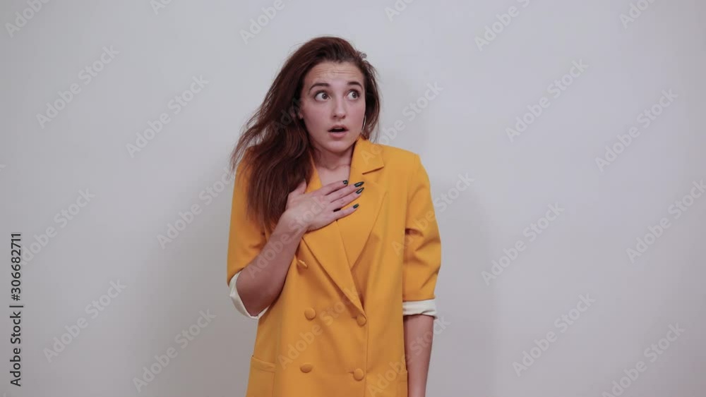Shocked young woman in yellow jacket isolated on gray background in studio keeping hands on chest, looking scary. People sincere emotions, lifestyle concept. Shocked young woman in yellow jacket isolated on gray background in studio keeping hands on chest, looking scary. People sincere emotions, lifestyle concept.