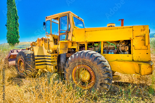 Side view of an yellow tractor in a high wheat field with rural landscape. The surrounding countryside with blue sky sunny day.