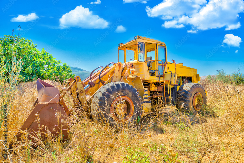 Side view of a yellow bulldozer on wheels for agriculture in a high wheat field with countryside landscape. Side view of a yellow bulldozer on wheels for agriculture in a high wheat field with countryside landscape.