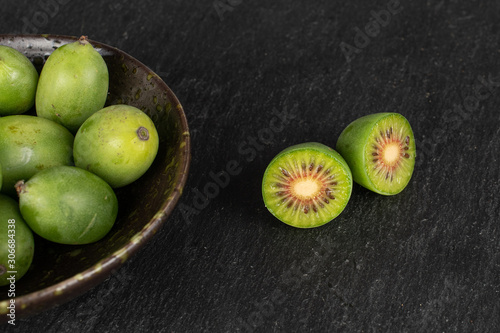 Group of lot of whole two halves of hardy green kiwi in glazed bowl on grey stone