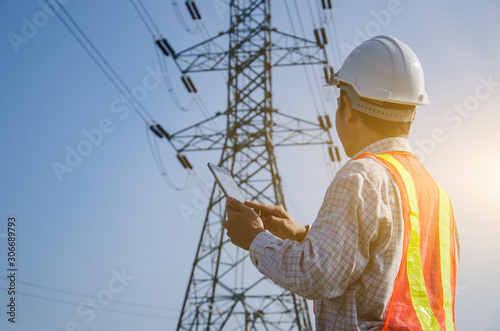 Electrical engineer holding and using a digital tablet with high voltage tower background.