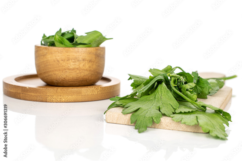 Lot of whole lot of pieces of fresh green parsley on round bamboo coaster in bamboo bowl on wooden cutting board isolated on white background