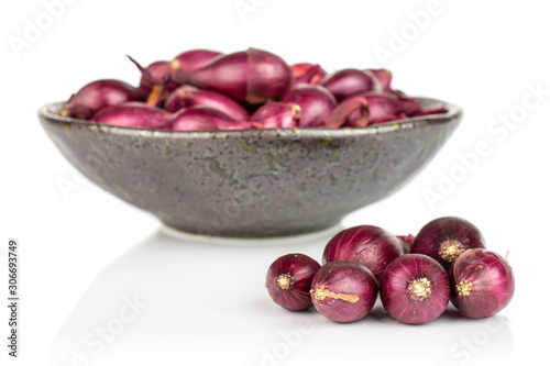 Lot of whole small red onion bulb in dark ceramic bowl isolated on white background