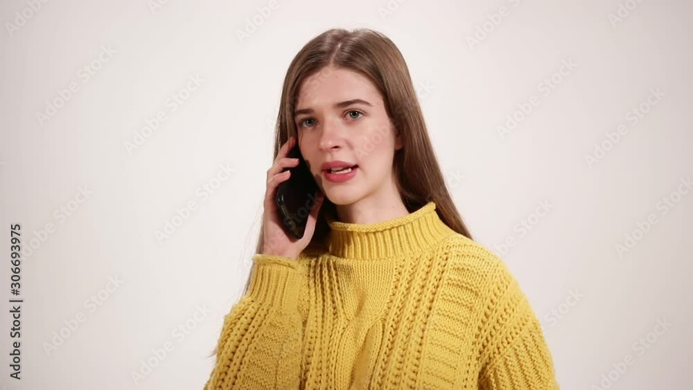Positive friendly girl in yellow sweater talking on her phone isolated over white background