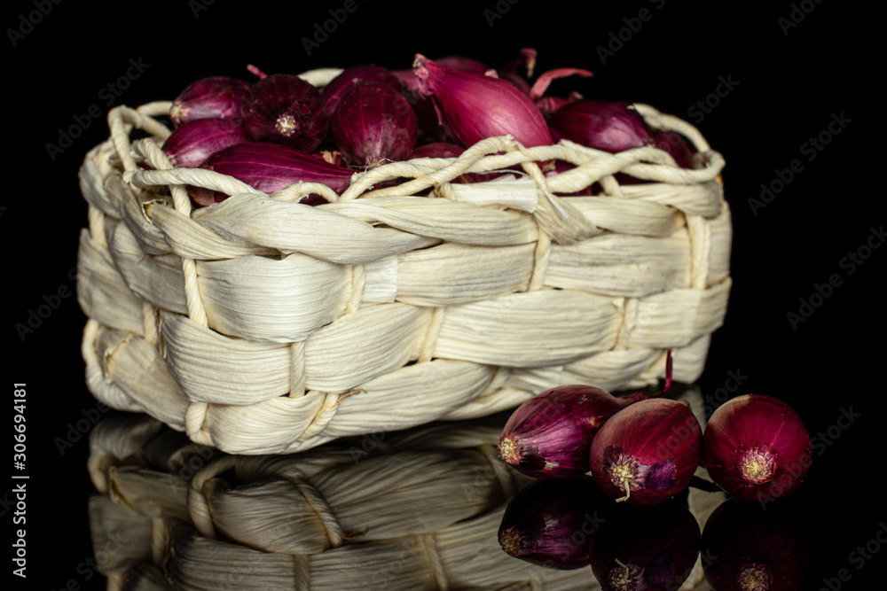 Lot of whole small red onion bulb in bast basket isolated on black glass