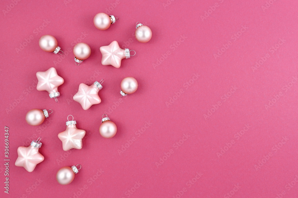Small light pink Christmas tree ornaments in shape of round ball baubles and stars on pink background with empty copy space on right side