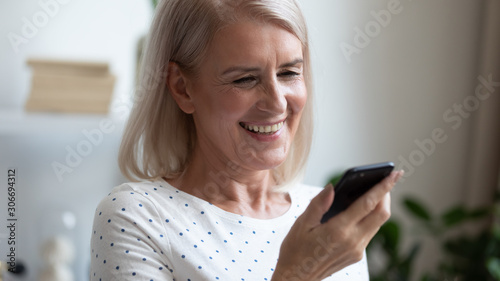 Aged woman holding smartphone looks at screen read pleasant sms