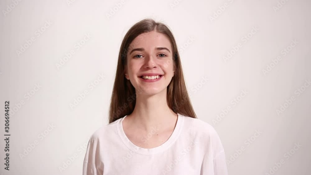 Girl in white t-shirt looks at the camera and starts to smile, white background Girl in white t-shirt looks at the camera and starts to smile, white background