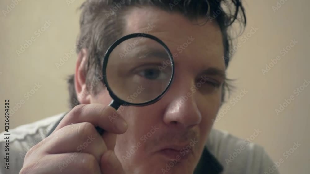 funny curious man looking at the camera through a magnifying glass.humorous video portrait funny curious man looking at the camera through a magnifying glass.humorous video portrait