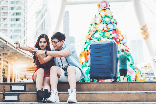 Couples  Asian tourists using mobile phones Take a selfie While they wait for the electric train on the station  with blur of christmas tree and tall building background  concept to young couples trav