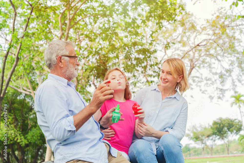 Grandparents with daughter enjoying time together in park. Daughter playing with blowing bubbles. Grandparents with daughter enjoying time together in park. Daughter playing with blowing bubbles.