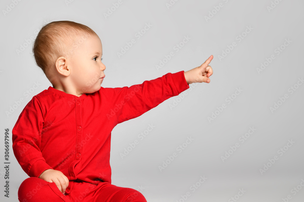 Little toddler boy points finger up side in red infant bodysuit with free text space on gray