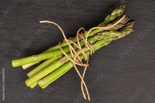 Lot of whole healthy green asparagus with straw rope flatlay on grey stone