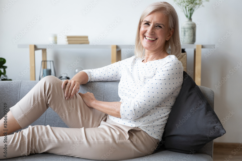Laughing aged woman sitting on comfy couch resting feels happy Laughing aged woman sitting on comfy couch resting feels happy