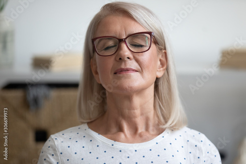 Closeup portrait calm aged woman closed eyes resting seated indoors