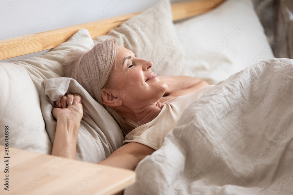 Satisfied middle-aged woman lying in bed enjoy early morning