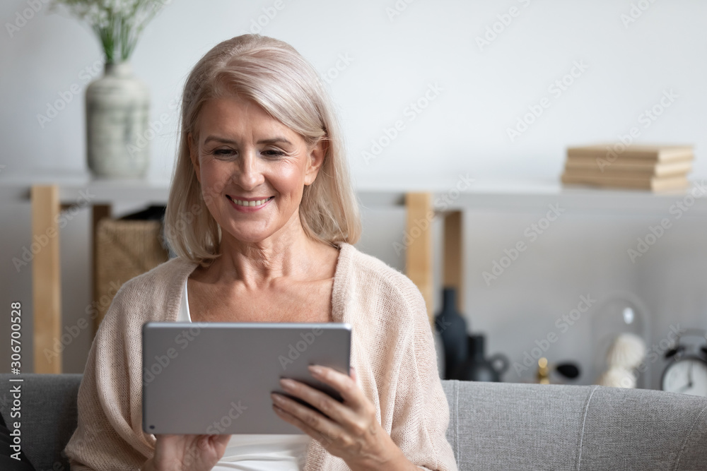 Attractive 60s woman sitting on couch with tablet computer Attractive 60s woman sitting on couch with tablet computer
