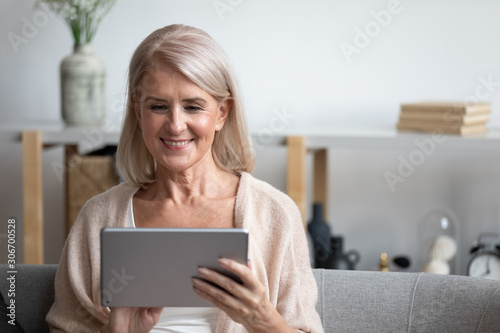 Attractive 60s woman sitting on couch with tablet computer