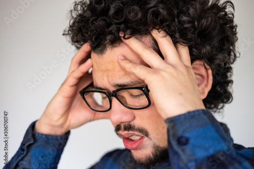 Latin American man with curly hair having a headache, upset expression, on a white background  