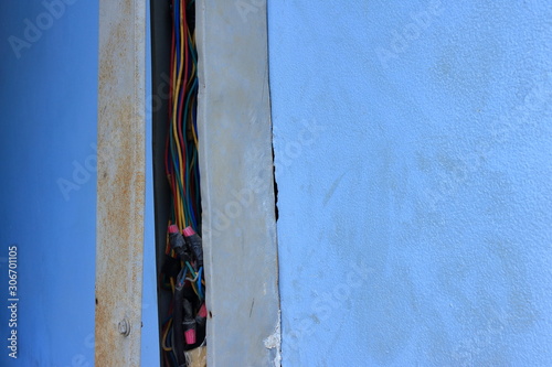 Closeup exposed power lines in broken wireway installed on dirty blue wall of a building photo