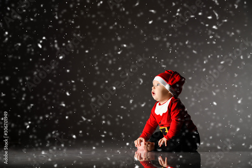 Smiling infant baby boy toddler in red christmas cap and new year costume is sitting on ice under the snow looking up © Dmitry Lobanov
