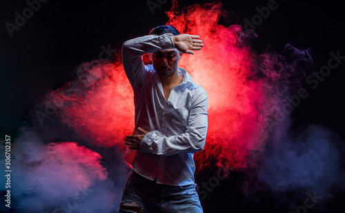 portrait of skillful caucasian man wearing white shirt move hands and arms during dance isolated over colorful smoky background