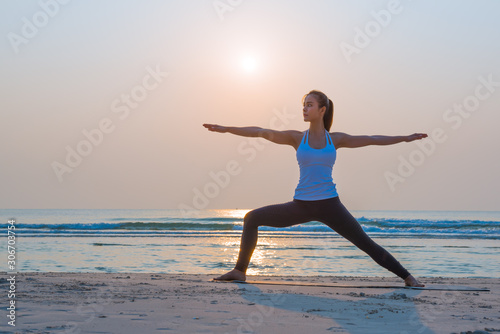 Yoga woman doing yoga warrior pose on the beach for wellbeing health lifestyle.