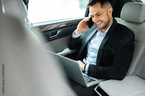 handsome young man sitting in his expensive car of top class, talking on phone and using laptop © alfa27