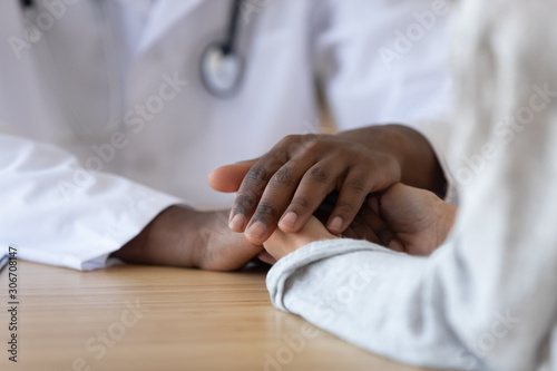 Young woman holding hands of african american male doctor, closeup.