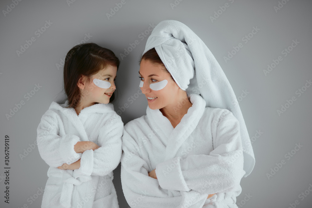 beautiful woman with her daughter stand isolated over grey background. parent and child together with eye patches