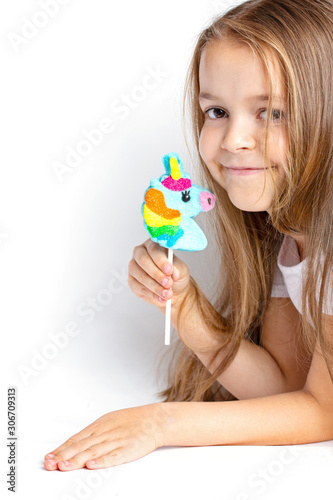 Joyful, happy child holds a unicorn lollipop in his hand on a white background. Close-up trend.