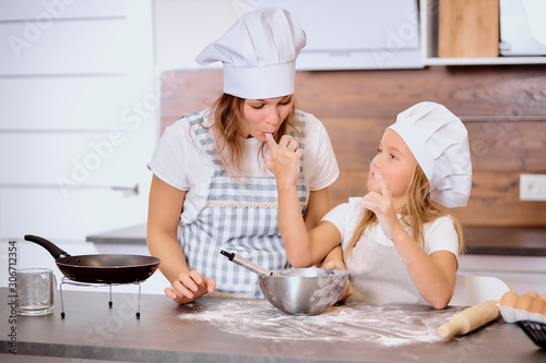 little girl with flour on finger give to mother to try, isolated in kitchen at home. mixing flour in bowl