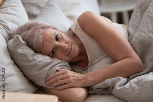 Sad elderly woman lying in bed suffers from insomnia