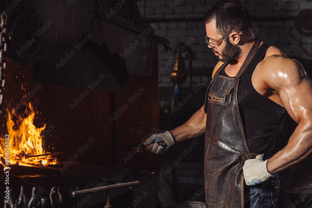 young bearded caucasian man blacksmith heating metal in furnace, have muscular body, bodybuilder work as forger, blacksmith young bearded caucasian man blacksmith heating metal in furnace, have muscular body, bodybuilder work as forger, blacksmith